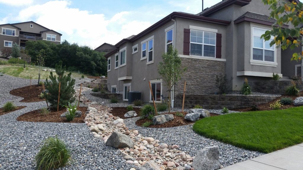 Backyard patio installation in Colorado Springs featuring natural stone surfaces, fire pit seating, drainage, and custom landscape design